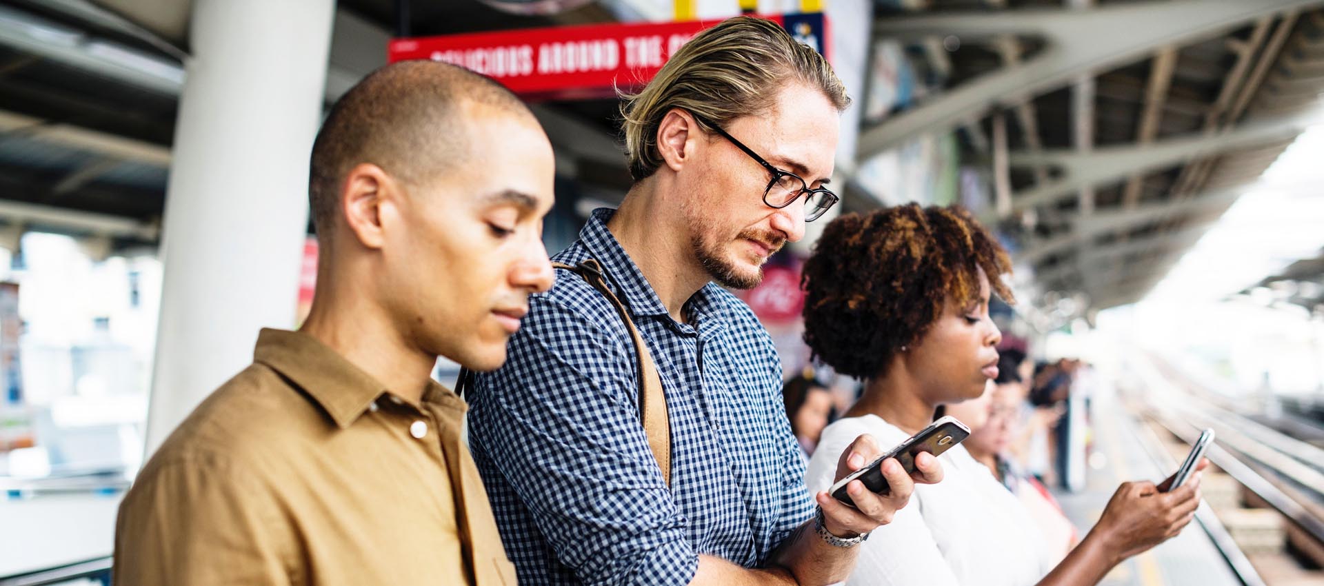 Three passengers at bus stop looking at their phones.