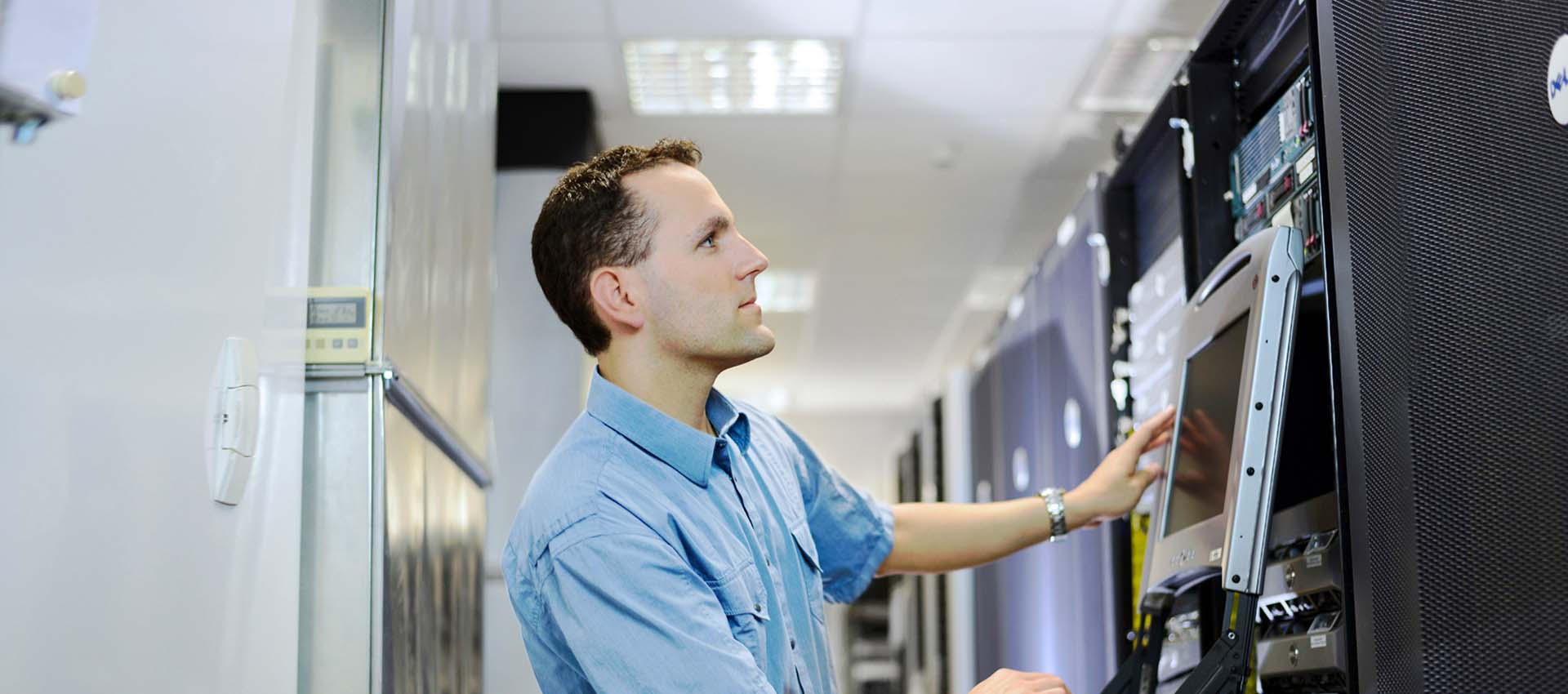 Man at wall of servers checking IT systems.