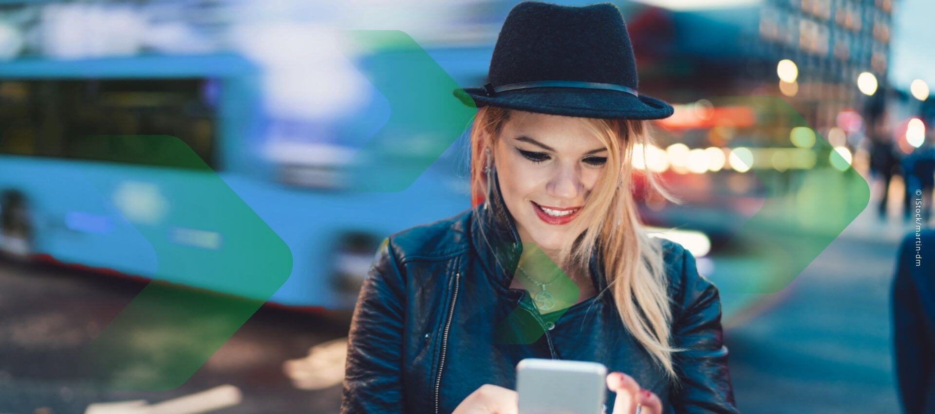 A woman wearing a hat and jacket is intently looking at her phone outdoors.